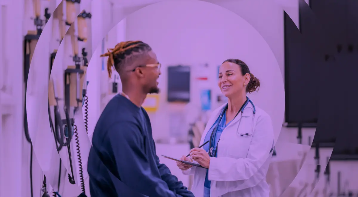 Un hombre sonriente con gafas habla con un médico que toma notas, en un contexto médico.